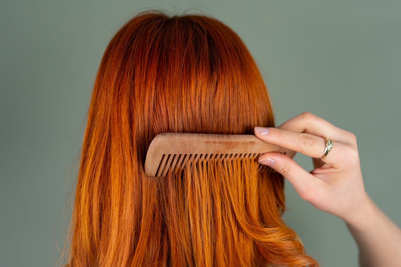 Close-up of a womans red hair being combed with a wooden comb, capturing the smooth texture.